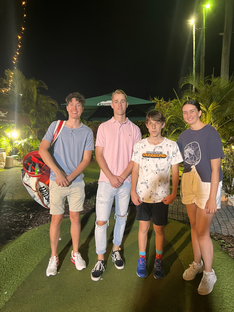 Four teens standing together at an otudoor minigolf venue.