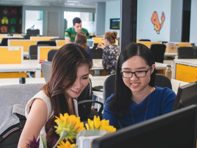 An employment readiness coach sits with a young autistic adult in an office, working together at a desk.
