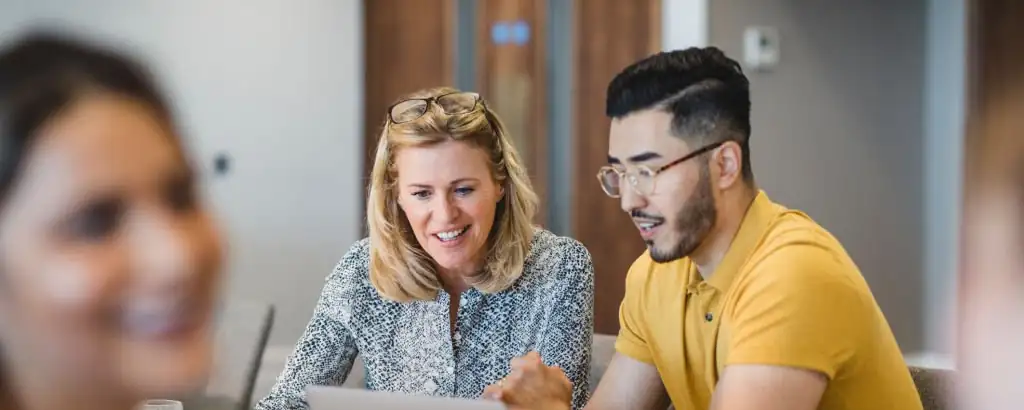 A middle aged white woman and an east asian man work together in an office environment.
