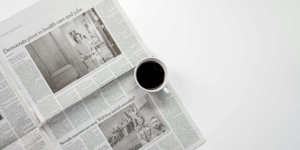 High angle photo of a cup of coffee and newspaper on a plain white desk.