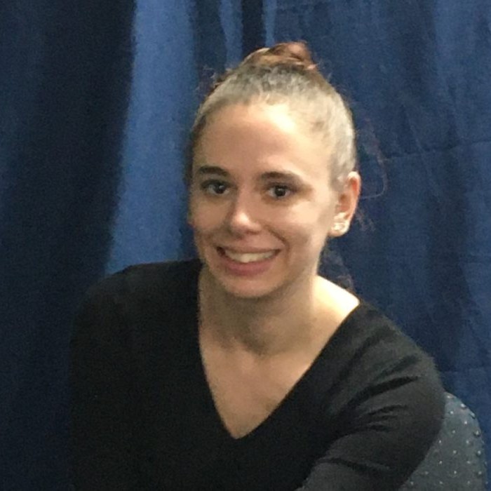 Mel Maddox. A Caucasian woman in her thirties, wearing a longsleeve black v-neck shirt with her hair in a high bun.