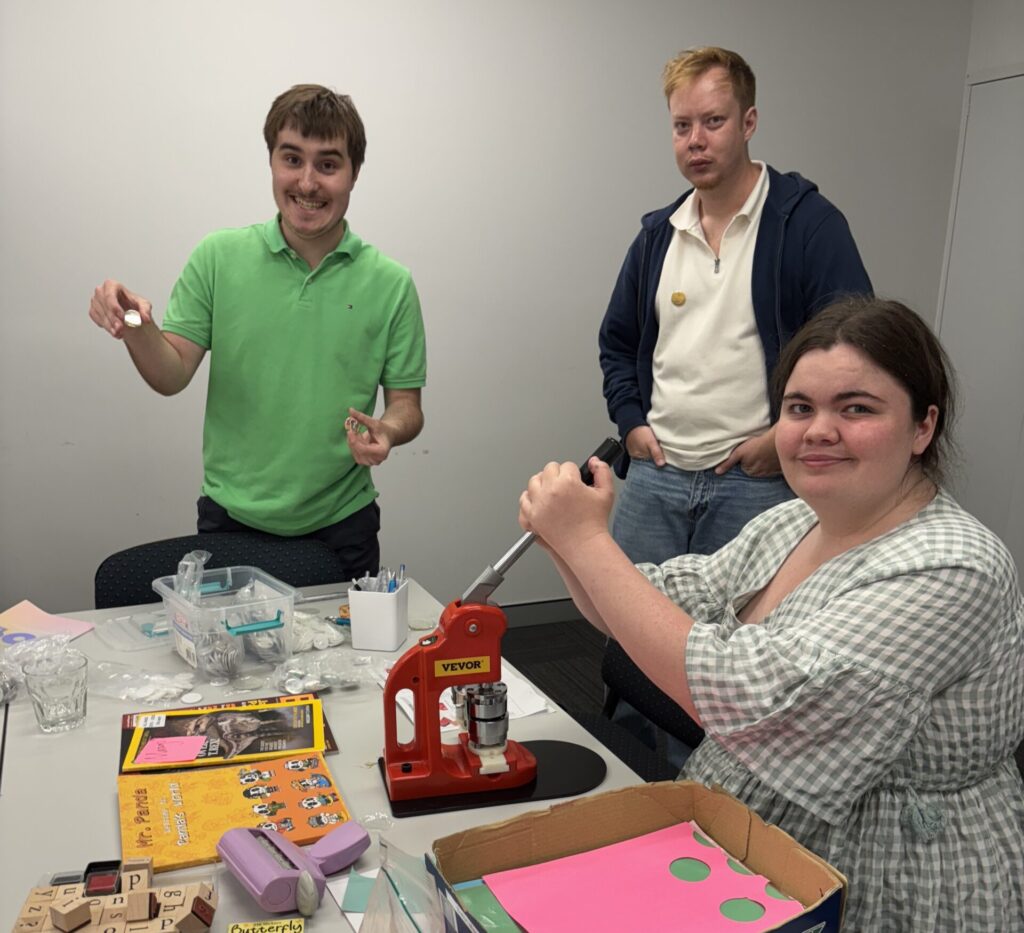 Three young Autistic adults, making buttons at an Empower Autism peer group.