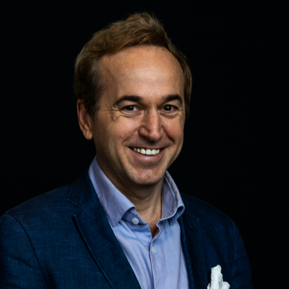 Casey Archbald, a tan Caucasian man in his thirties, wearing a navy blue collared shirt and suit jacket.