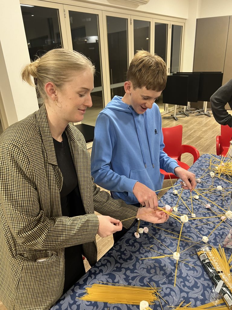 A volunteer, Georgina, builds a marshmallow and spagetthi tower with an Autistic teen boy, at a peer group.