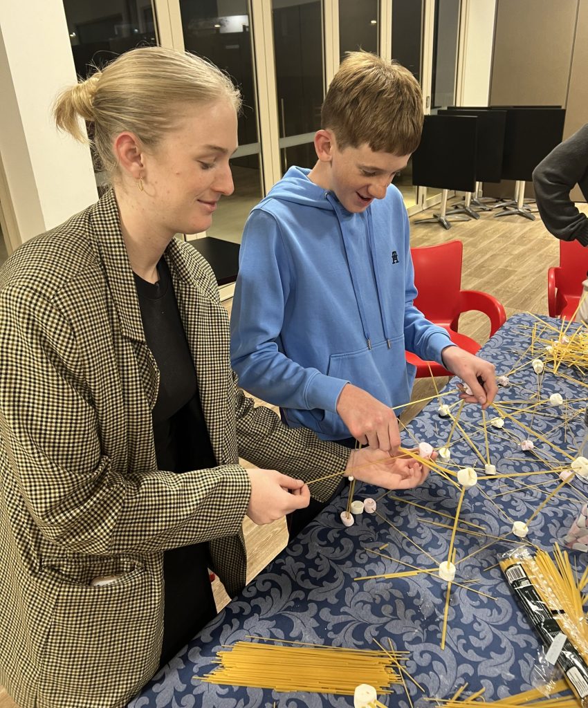 A volunteer, Georgina, builds a marshmallow and spagetthi tower with an Autistic teen boy, at a peer group.