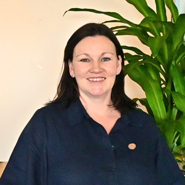 Holly, a middle aged Scottish woman with a kind smile and shoulder length dark hair.