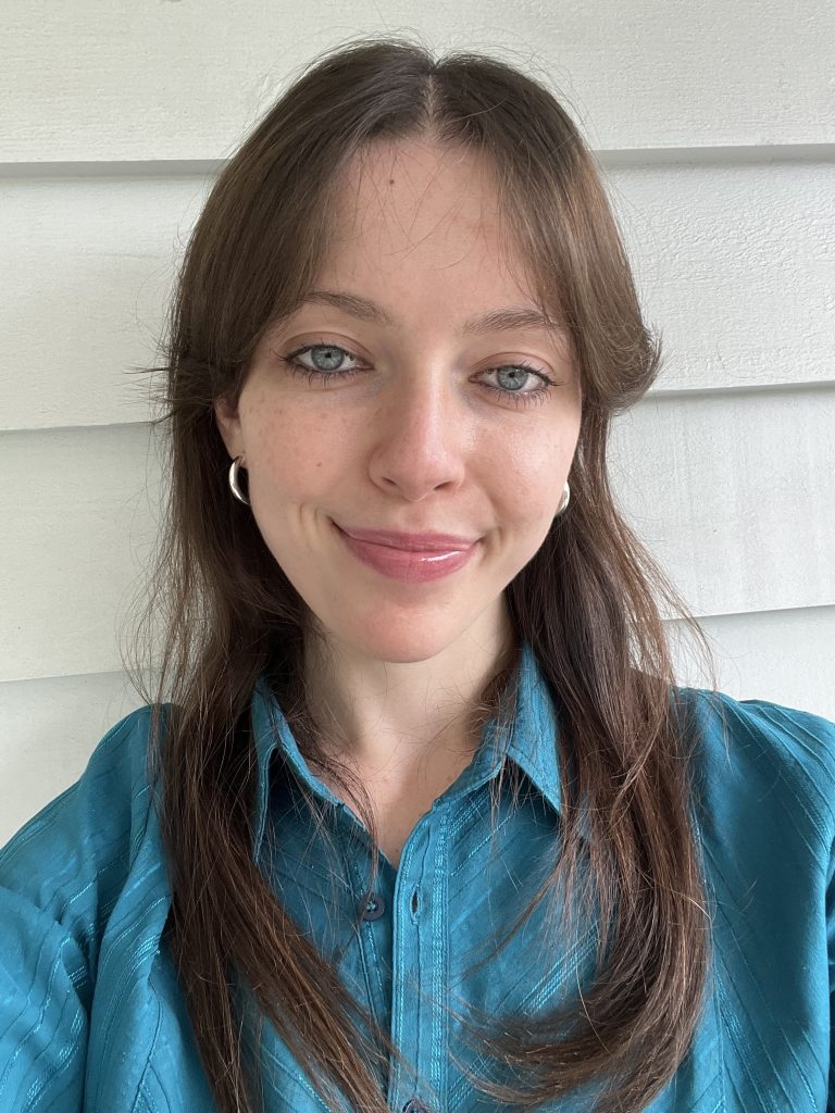 Selfie of Maddy, a young white woman with long hair, wearing a turquoise button-up and large hoop earrings.